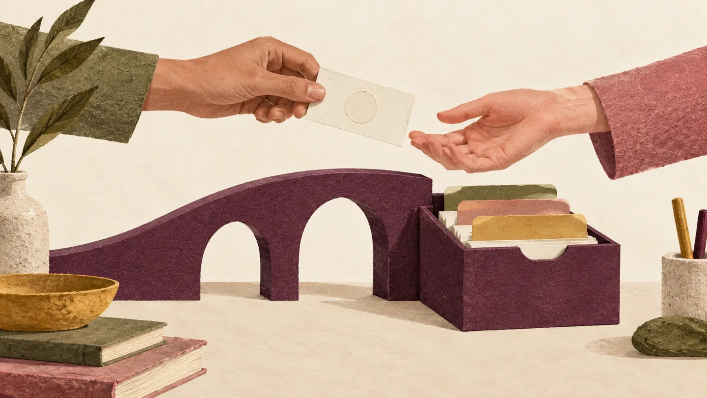 Hands pass a blank contact card across a paper bridge into an organized card-file box.